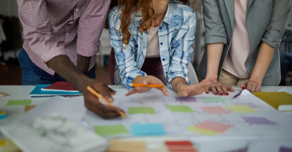 A team of three people using sticky notes and paper to organize a project from planning to delivery.